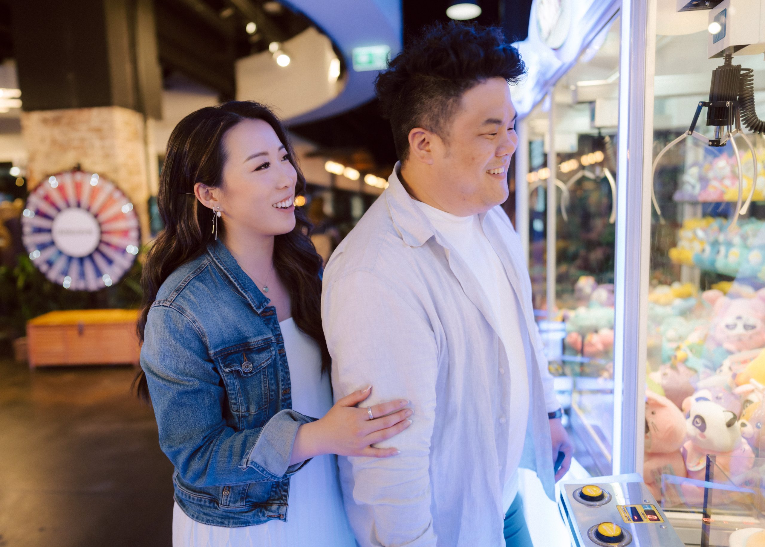Couple at an arcade playing a game with neon lighting surrounding them for a pre wedding photoshoot.