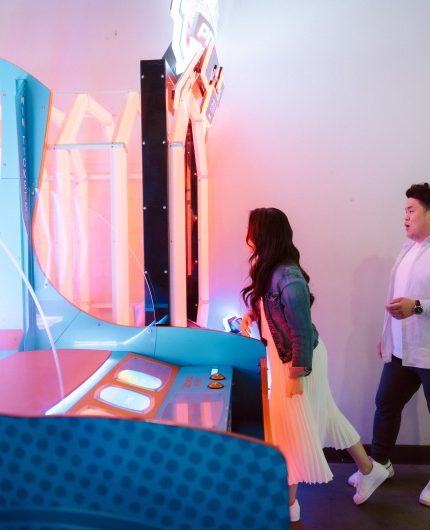 Couple at an arcade playing a game with neon lighting surrounding them for a pre wedding photoshoot.